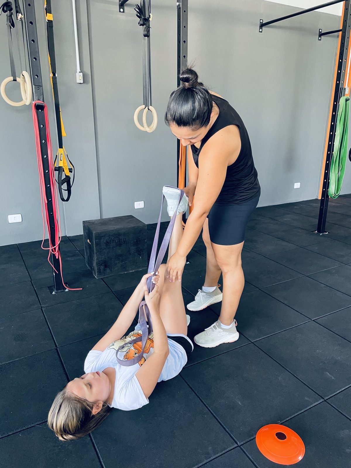 Professora ajudando uma aluna em um alongamento com faixa elástica